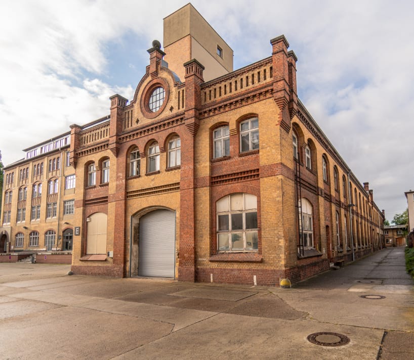 Historisches Backsteingebäude mit großem Tor und Fenstern bei bewölktem Himmel.