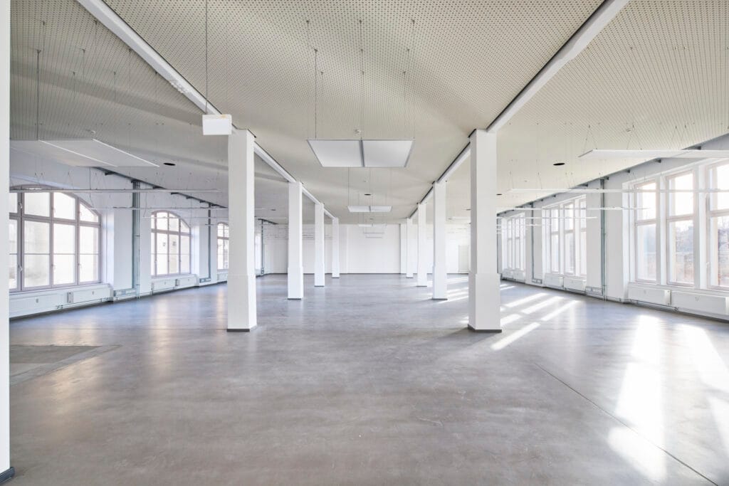 Geräumiges, leeres Loft mit großen Fenstern und moderner Beleuchtung in einem Gebäude.