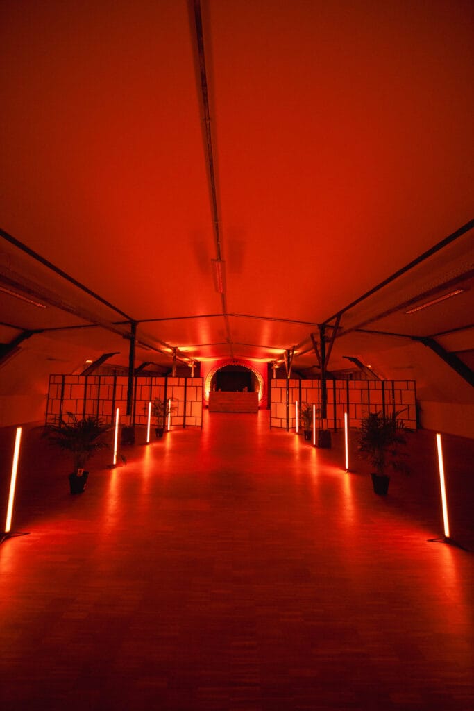 Ein roter, beleuchteter Innenraum mit moderner Architektur und dekorativen Pflanzen.