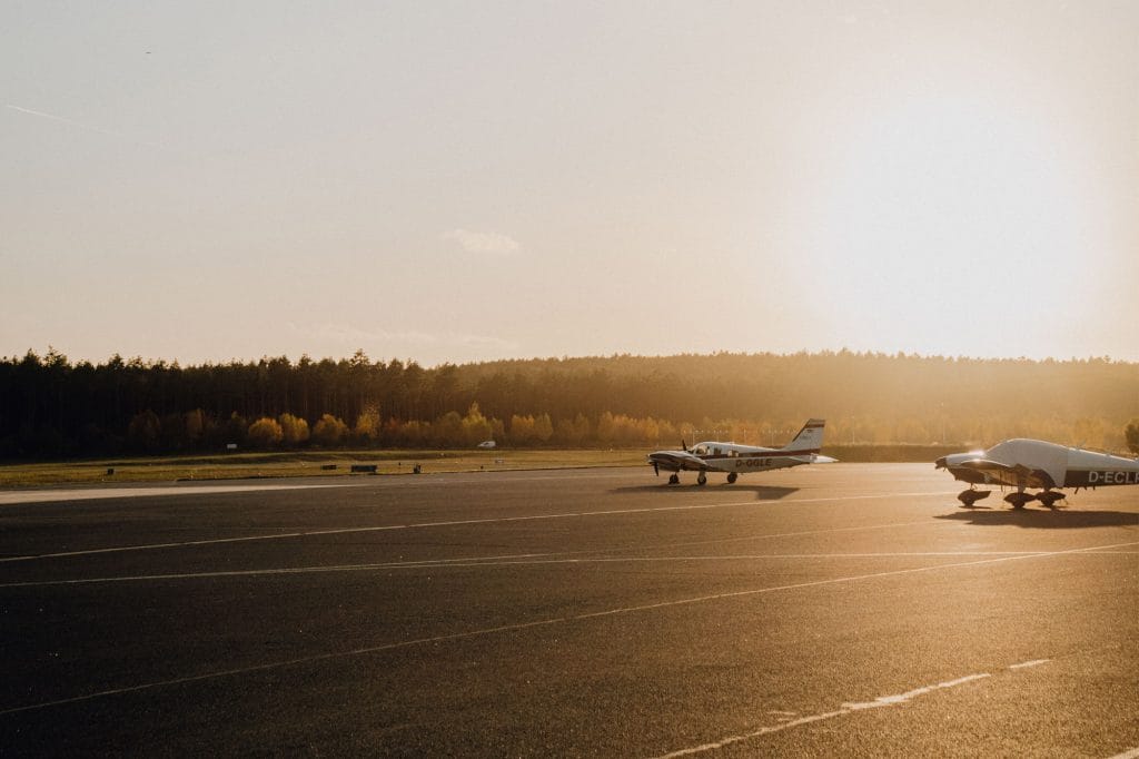 Zwei Flugzeuge auf der Landebahn bei Sonnenuntergang, umgeben von Bäumen.