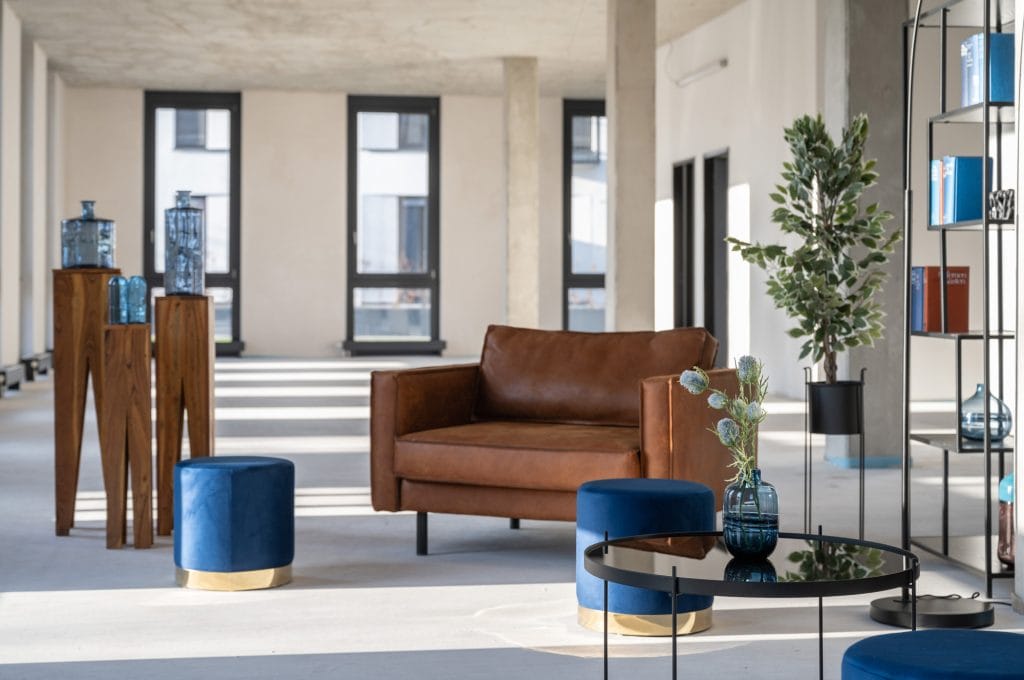 Moderner Raum mit braunem Ledersofa, blauen Hockern und dekorativen blauen Glasvasen.