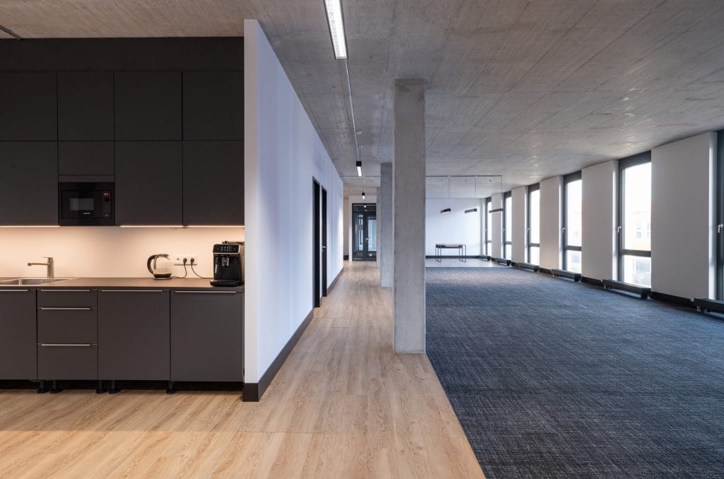Moderner Büroraum mit Teeküche und großen Fenstern für natürliche Beleuchtung.