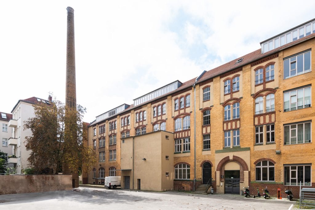 Moderner Loft-Wohnbereich mit blauer Couch, Holz-Tisch und Rattanstühlen auf Betonboden.