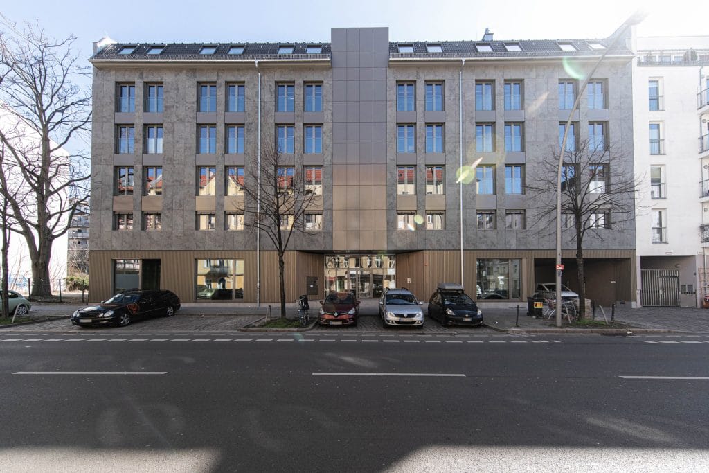 Moderne Bürogebäude-Fassade mit parkenden Autos in städtischer Umgebung bei Sonnenschein.