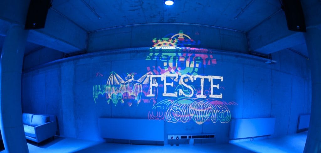 Graffiti-Kunst mit Fledermaus-Motiv und Feste an Betonwand in blauer Beleuchtung.