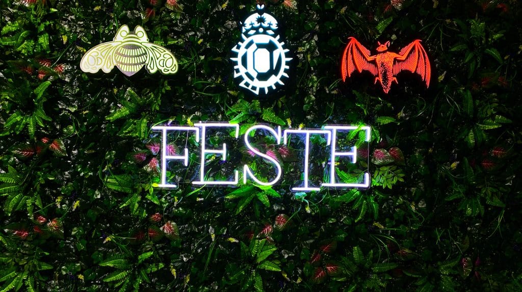 Neon-Schriftzug FESTE umgeben von leuchtenden Symbolen auf grünem Hintergrund.