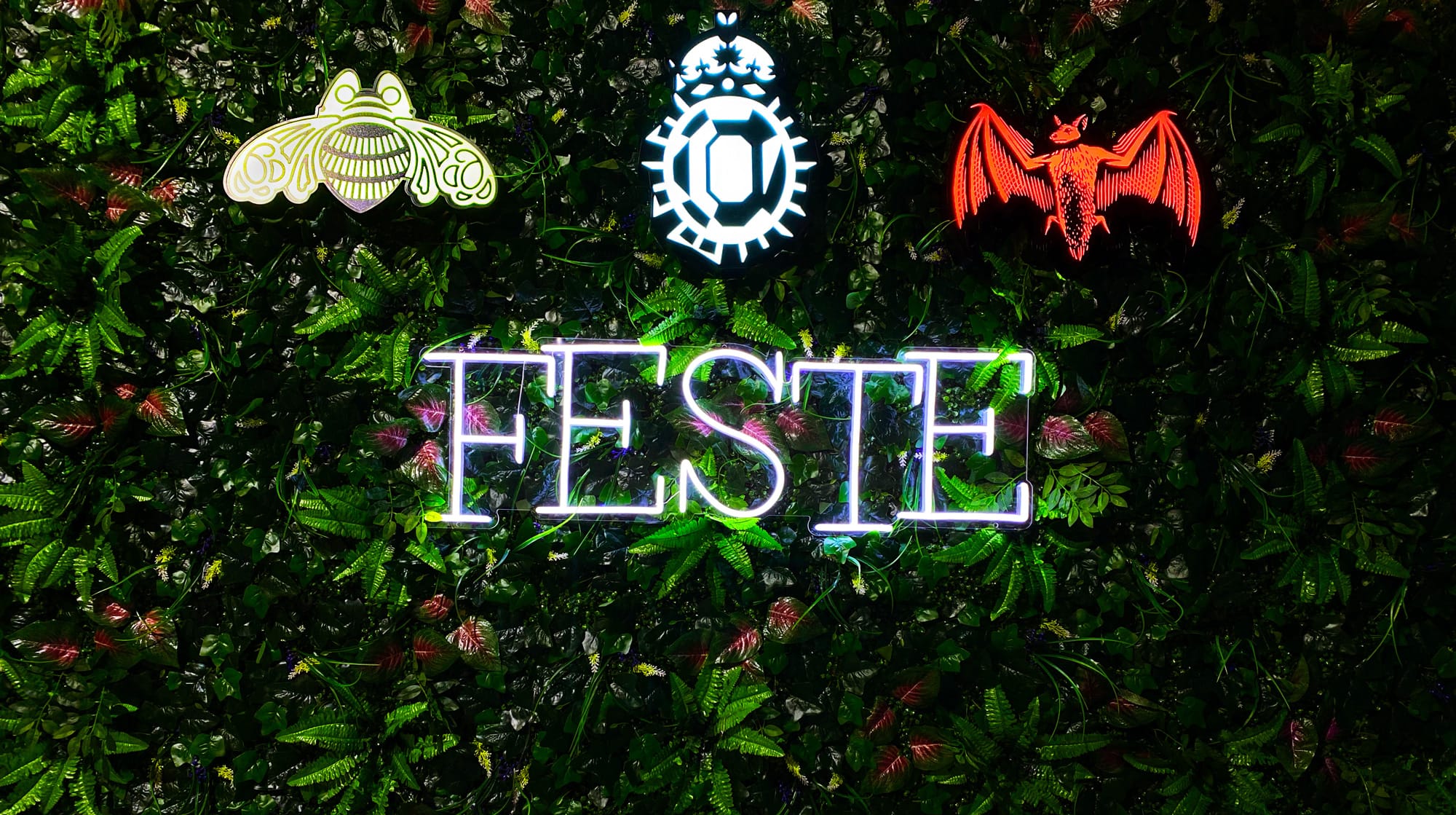 Neon-Schriftzug FESTE umgeben von leuchtenden Symbolen auf grünem Hintergrund.