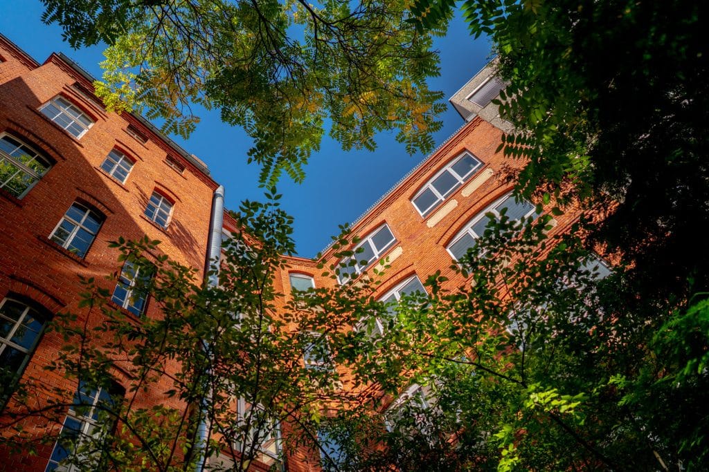 Backstein-Gebäude mit grünen Bäumen und blauem Himmel, von unten fotografiert.