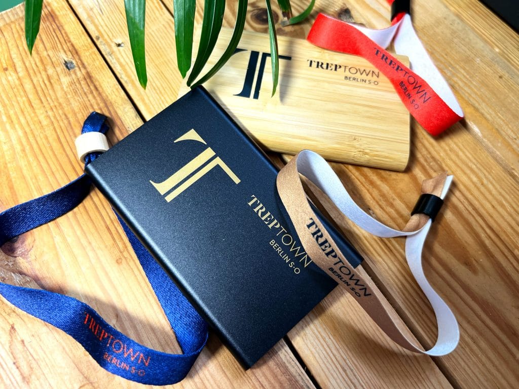 Modische Armbänder und Holzbrett mit Treptown-Logo auf Holzoberfläche unter Blättern.