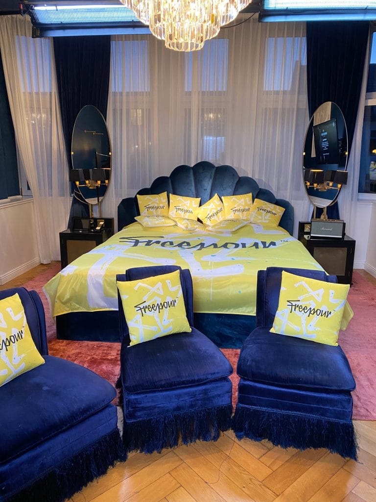 Luxuriöses Schlafzimmer mit gelben Kissen und blauen Sesseln unter einem eleganten Kronleuchter.