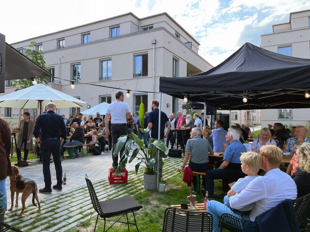 Grillfest im Garten mit Gästen, Pavillons und fröhlicher Atmosphäre bei sonnigem Wetter.