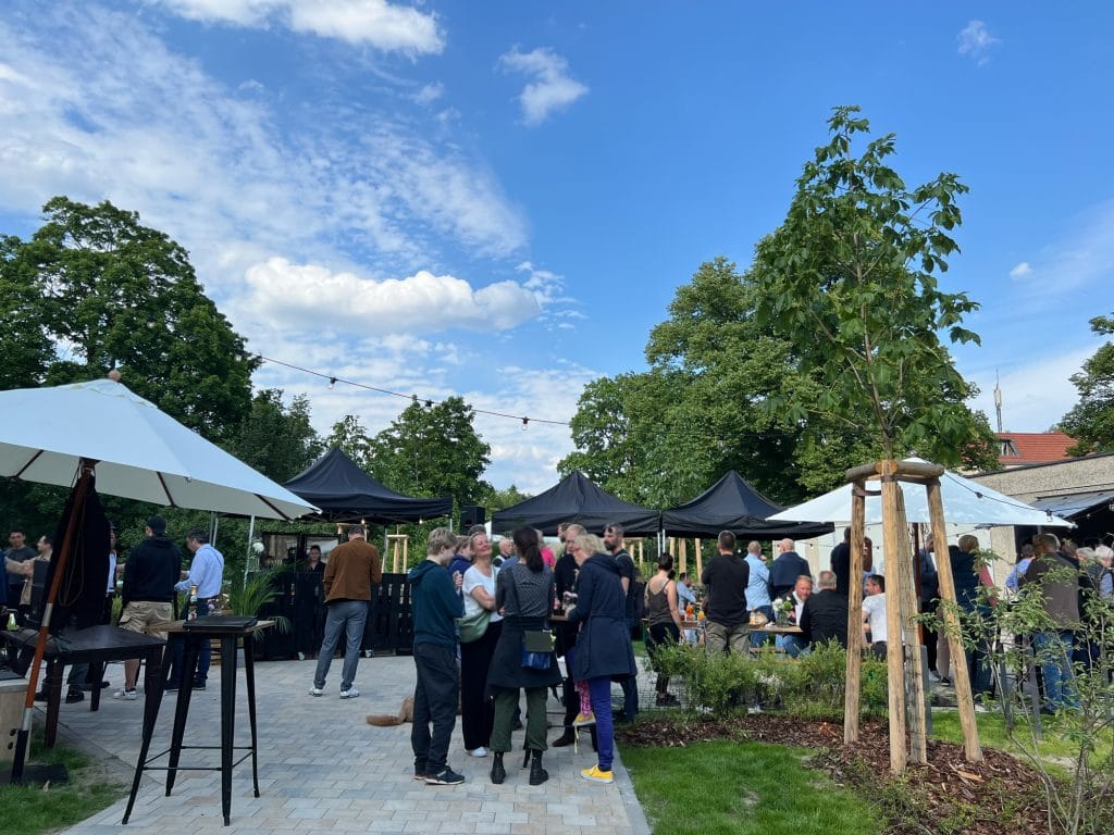 Geselliges Treffen im Freien unter blauem Himmel mit Sonnenschirmen und Bäumen.