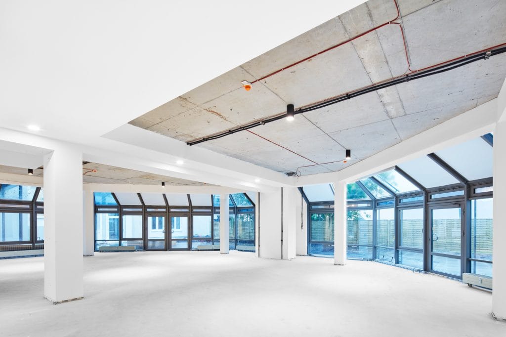 Großer, leerer, heller Raum mit Betonwänden und großen Glasfenstern, minimalistisch gestaltet.