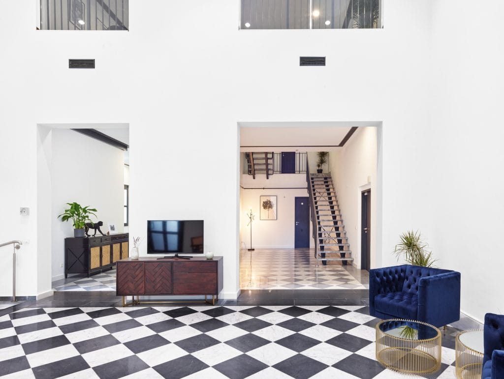 Moderner Wohnzimmerbereich mit Schachbrettfliesen, blauen Sesseln und Treppenaufgang.