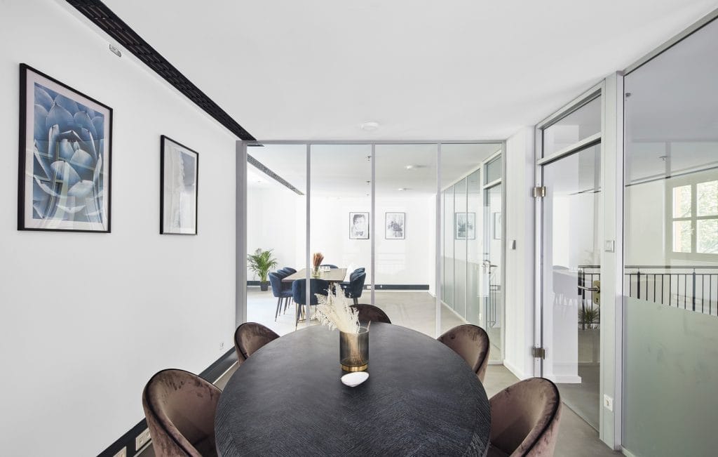 Moderner Konferenzraum mit runden Tischen, Pflanzen, Glaswänden und Kunstwerken an den Wänden.