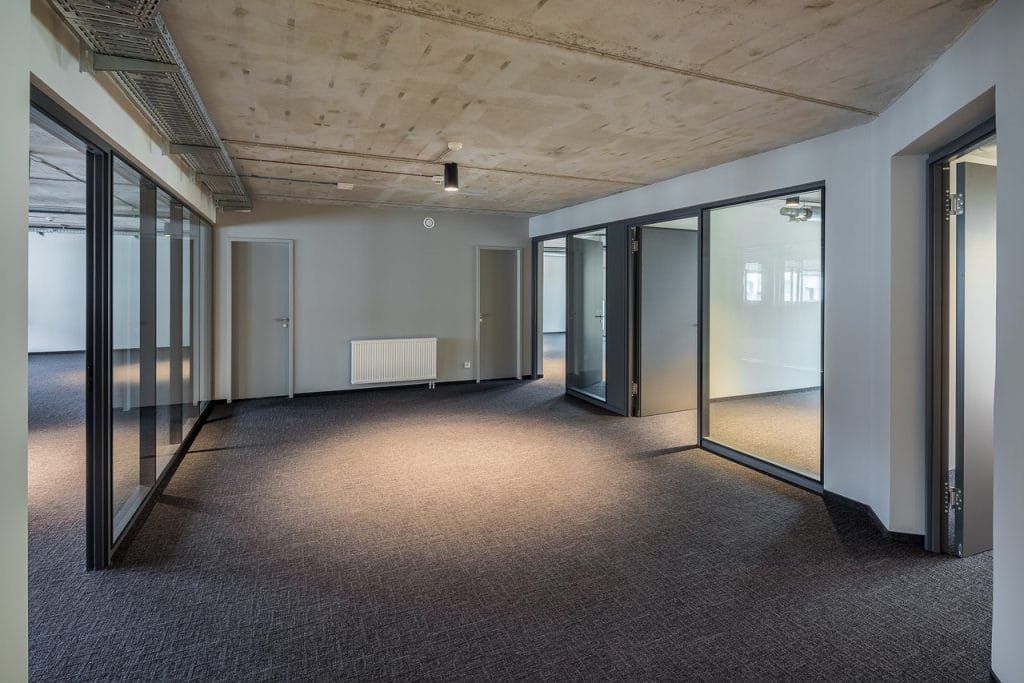 Moderner, leerer Büroraum mit großen Glaswänden und grauem Teppichboden.