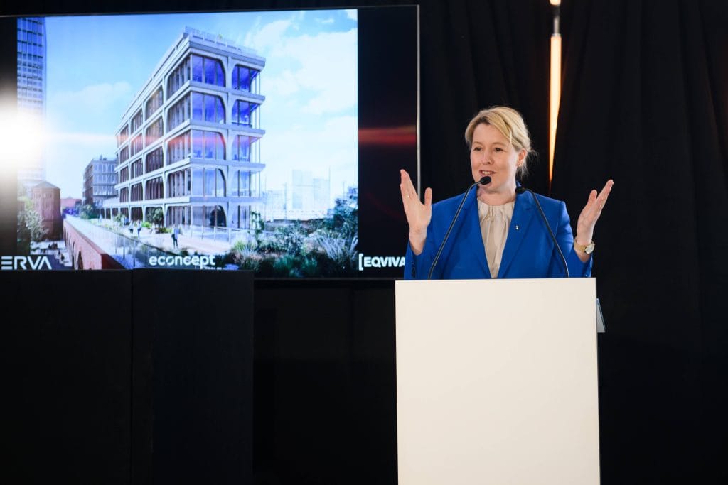 Ein Redner präsentiert ein Bauprojekt auf einer Bühne vor Publikum.