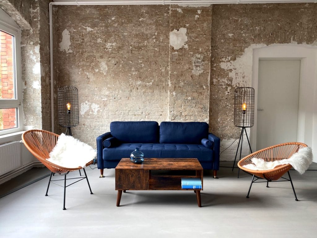 Moderner Wohnraum mit blauer Couch, Holz-Couchtisch und industrieller Backsteinwand.