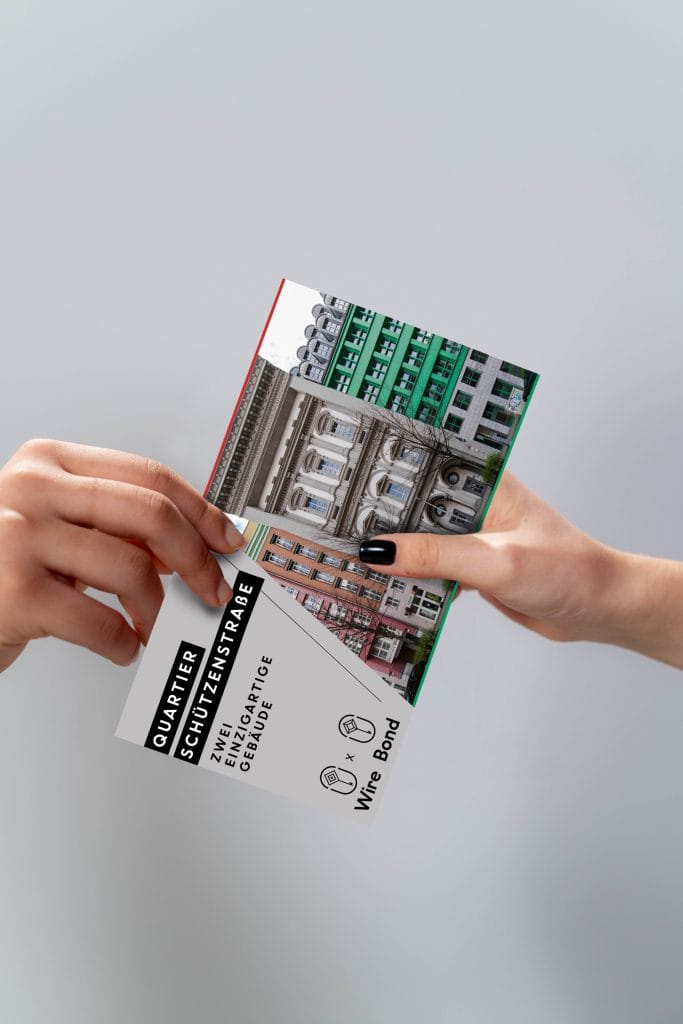 Zwei Hände halten Quartier-Schützenstraße-Postkarte mit Gebäudebildern und Text.