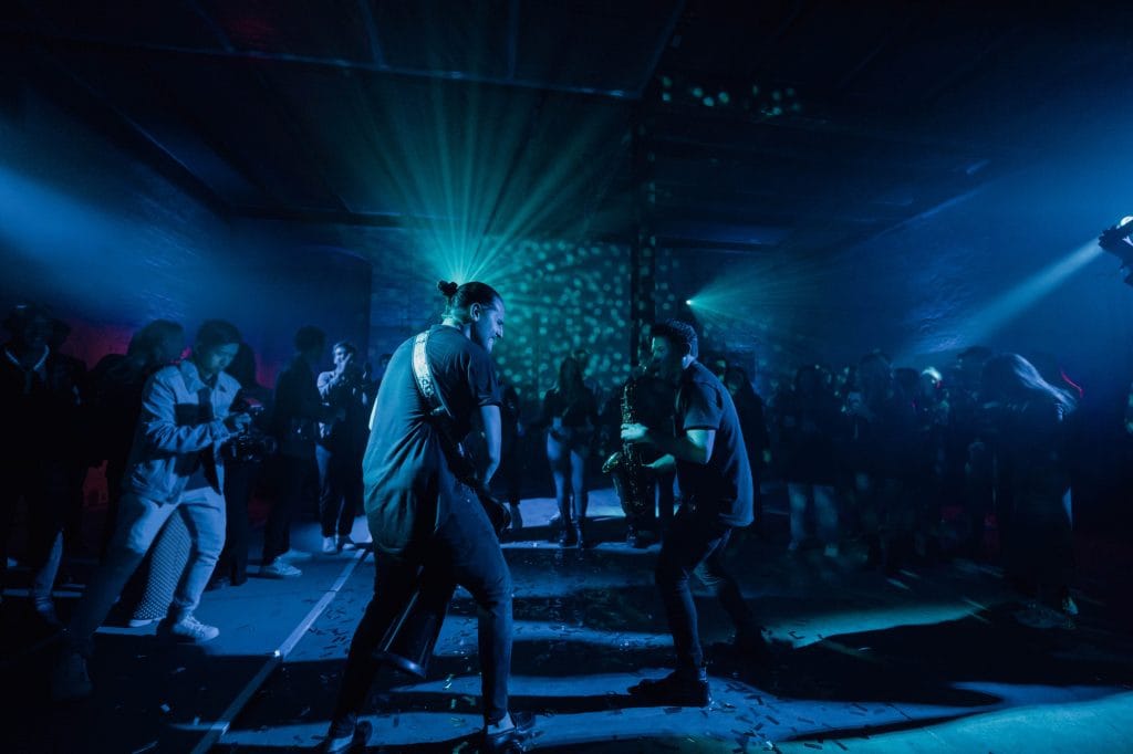 Musiker spielen Gitarre und Saxophon auf einer Bühne in blauem Licht.