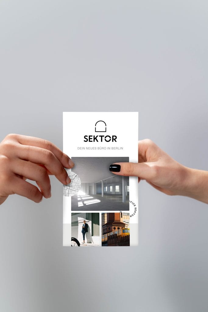 Zwei Hände halten ein Werbeflyer für ein neues Büro in Berlin, Sektor.