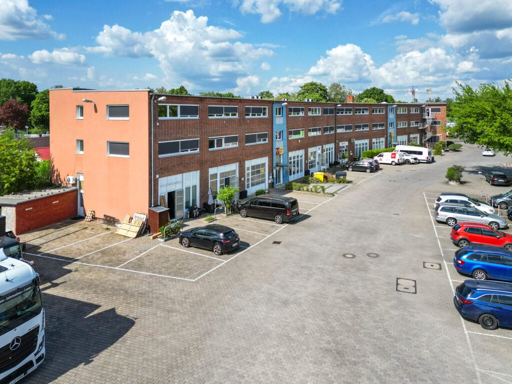 Gewerbegebäude mit Parkplatz bei sonnigem Wetter und blauem Himmel im Hintergrund.