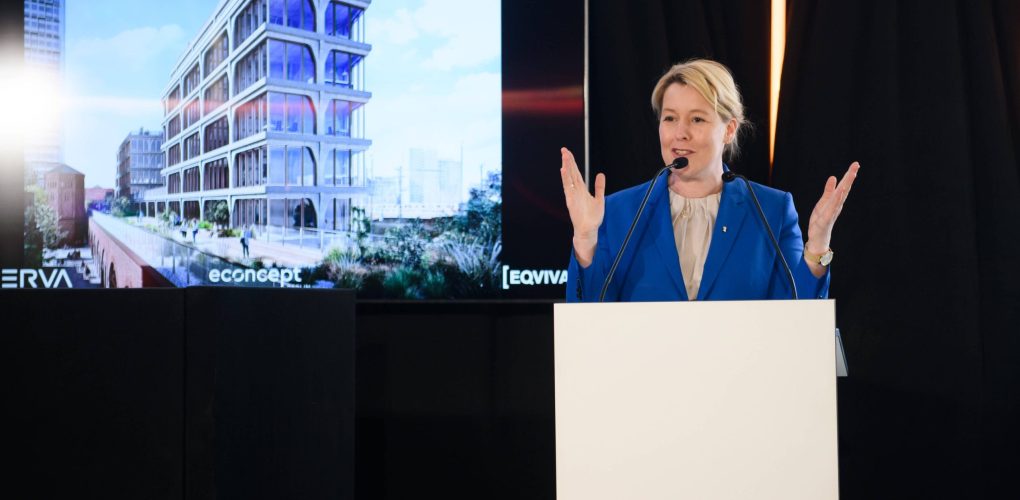 Ein Redner präsentiert ein Bauprojekt auf einer Bühne vor Publikum.